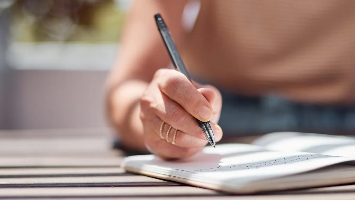Gros plan sur une main de femme qui écrit avec un stylo dans un journal intime.