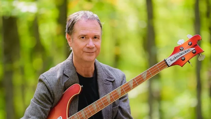 François Pérusse est assis dans le bois en tenant une basse.