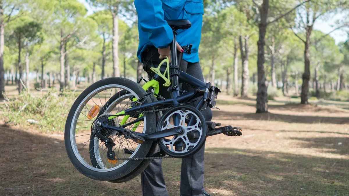 Une personne transporte un vélo pliable dans le bois.