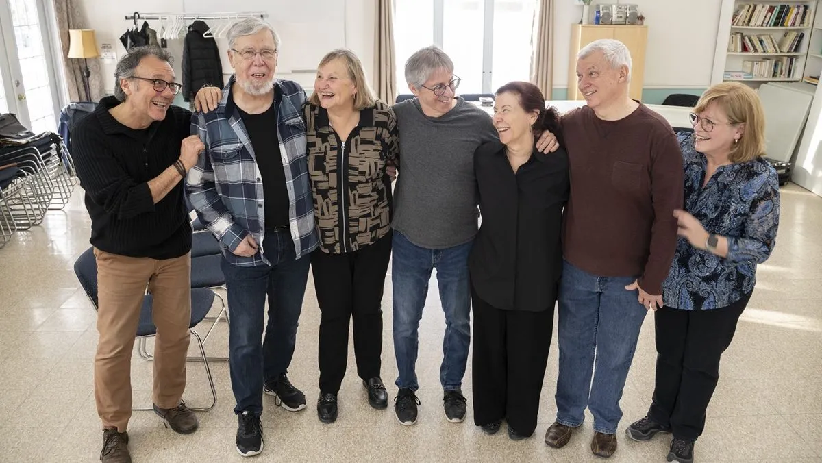 Sept membres d'une troupe de théâtre amateur posent en rang dans une salle communautaire.