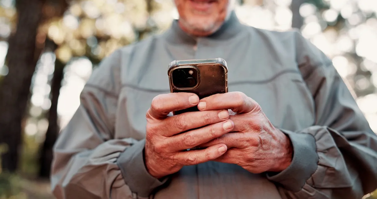 andonneur utilisant un téléphone intelligent pour accéder à une application de randonnée en forêt.